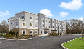 East Greenwich apartment for rent - A large grey building with a parking lot in front.