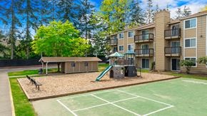 Everett apartment for rent - A playground with a slide and a basketball court in front of Hillcrest apartment buildings.