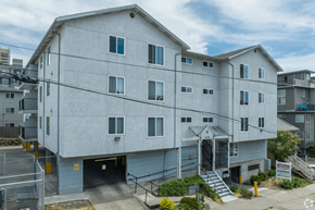 Seattle apartment for rent - A large white building with a garage door and stairs leading to the entrance.