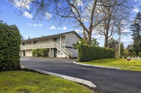 Lakewood apartment for rent - A building with a grey roof and white walls is surrounded by greenery.