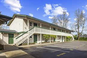 Lakewood apartment for rent - A white building with green doors and windows is surrounded by a parking lot.