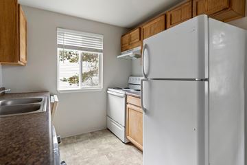 Lakewood apartment for rent - A white refrigerator stands in a kitchen with wooden cabinets and a window with blinds.