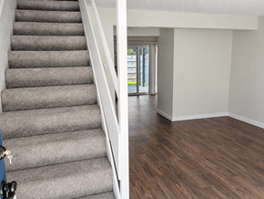 Sumner townhouse for rent - A staircase with a grey carpeted runner and white handrail leads to a bright room with a wooden floor and a glass door.