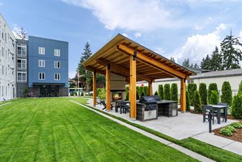 A wooden pavilion is surrounded by a grassy area and a patio with a grill