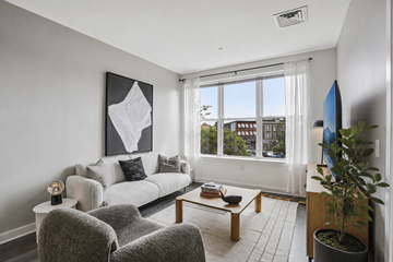 Montclair apartment for rent - A living room with a grey couch, a grey chair, a coffee table, a potted plant, and a painting on the wall.