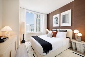 New Rochelle apartment for rent - A bedroom with a large bed, a nightstand, and a window with a view of the city.