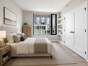 Arlington apartment for rent - A bedroom with a large bed and a view of a cityscape through the window.