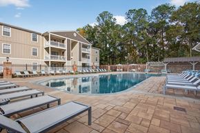 Ocean Springs apartment for rent - A large swimming pool surrounded by lounge chairs and a building in the background.
