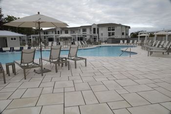 A pool area with chairs and umbrellas in front of a building