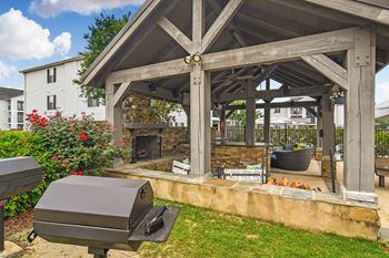 A wooden gazebo with a grill and a fire pit in the middle of a grassy area