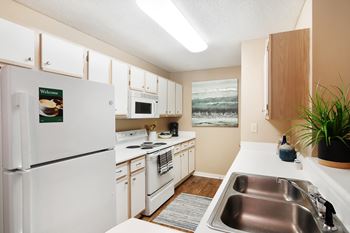A kitchen with a white refrigerator and a sink and microwave