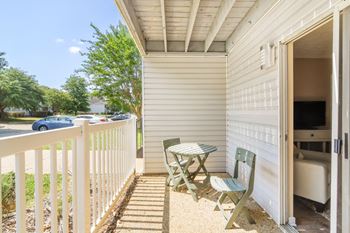 A small table and two chairs sit on a balcony in front of a parking lot