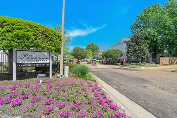 The entrance to a park with purple flowers and a sign