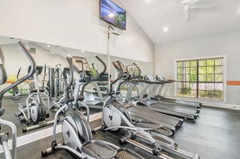 A gym with a row of stationary bikes and a television mounted on the wall 