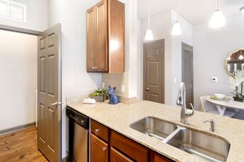 A kitchen with a dishwasher, sink and a quartz counter top with wooden cabinets