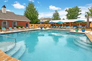 A large outdoor swimming pool with a sun lounger and umbrellas