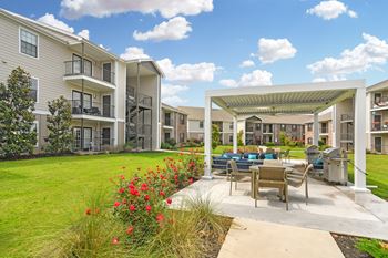 Outdoor lounge and grill patio with grass and tables and chairs at parkwest apartment homes in flowood mississippi