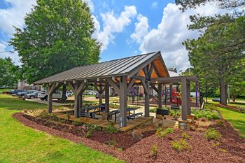 A pavilion with a metal roof and wooden pillars is surrounded by a garden with a variety of plants and flowers