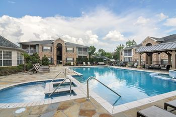 A swimming pool surrounded by a patio with chairs and a building in the background