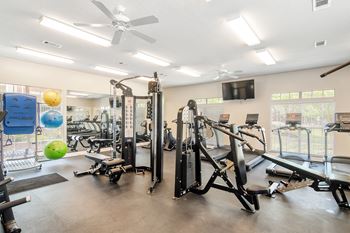 A gym with cardio machines and weights and a tv