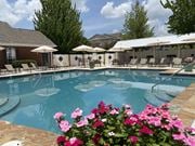 Shreveport apartment for rent - A pool surrounded by chairs and umbrellas with flowers in the foreground.