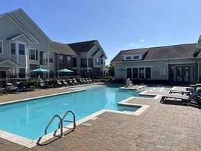 Zachary apartment for rent - A swimming pool surrounded by lounge chairs and umbrellas in front of apartment buildings at Audubon Park Apartment Homes, Zachary, Louisiana