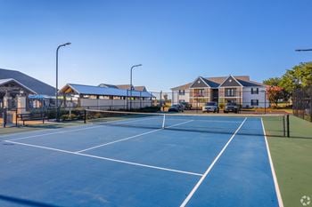 A tennis court with a blue surface and white lines, surrounded by a fence and a building in the background