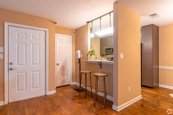 A kitchen area with a bar stool and a counter with hardwood floors