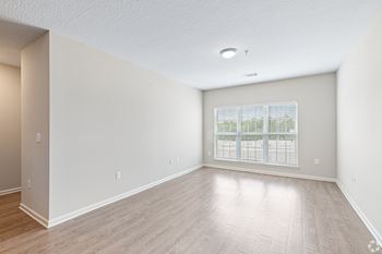 An empty living room with a large window and wood flooring 