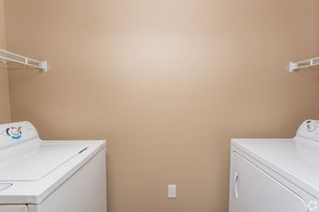 Two white washing machines in a room with beige walls