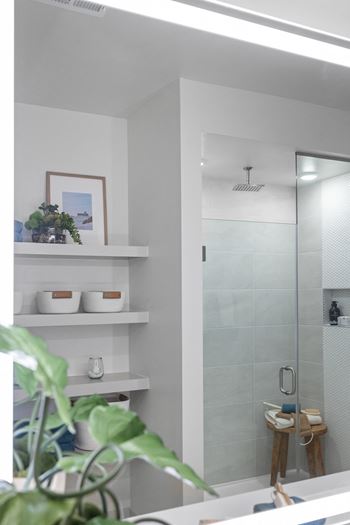 A bathroom with a glass shower door and a white counter.