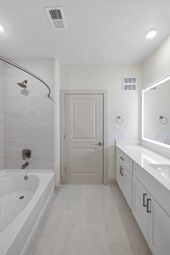A white bathroom with a tub, sink, and mirror.