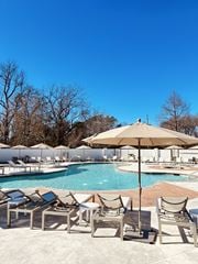 Tyler apartment for rent - A pool with chairs and umbrellas is surrounded by trees.