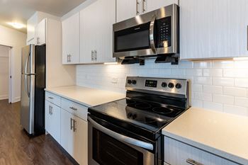 A kitchen with white cabinets, stainless steel appliances and modern tile backsplash