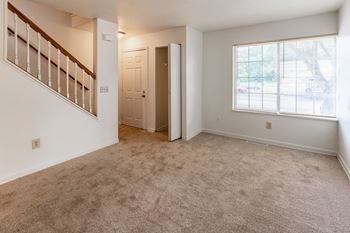 An empty living room with carpet and a door to a bedroom