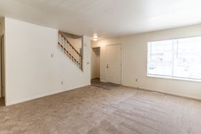 Battle Creek townhouse for rent - A cozy living room with a large window and carpeted flooring by a staircase at Arbor Pointe Townhomes Apartments, Battle Creek, MI