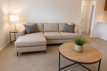 Greenwood apartment for rent - A living room with a beige couch, a small table with a plant on it, and a lamp on a side table.