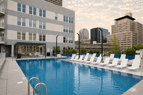 Indianapolis apartment for rent - A large swimming pool with white chairs and a building in the background at The Whit Apartments, Indianapolis, IN, 46204