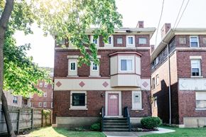 Pittsburgh apartment for rent - A red brick house with a pink door and a small porch.