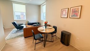Pittsburgh apartment for rent - A living room with a brown couch, a blue chair, a small table with chairs, and two framed pictures on the wall.at The Jones Tower at the Collective, Pittsburgh, PA 15203