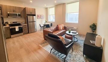 Pittsburgh apartment for rent - A modern kitchen and living room with a brown leather couch and a wooden floor.