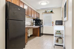 Memphis apartment for rent - A black refrigerator stands in a kitchen with wooden cabinets and a white shelf.