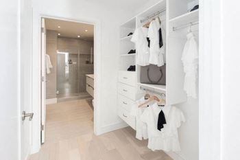 A white closet with clothes hanging and a bathroom in the background.