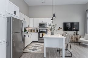 Liberty Township apartment for rent - Liberty Township, OH, Apartments Near Paul Brown Stadium - Liberty Center - Modern Kitchen with Vinyl Wood Plank Flooring, Stainless Steel Appliances, White Quartz Countertops, White Cabinetry, Tile Backplash, Moveable Island with Grey Chairs, Pendant Lights, and Access to Living Room.