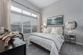 Liberty Township apartment for rent - One-bedroom Apartments in West Chester OH - Liberty Center - Furnished Bedroom with Grey Shaw Carpeting, Round Coffee Tables with Lamps, Circular FRamed Mirrors, Chair, Wooden Dresser, Window