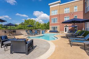Cincinnati apartment for rent - A pool surrounded by chairs and umbrellas with a building in the background.