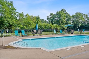 Swimming pool with blue chairs and umbrellas and a black fence around it