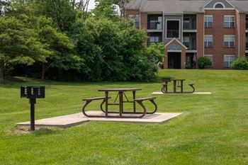 A picnic table and two benches in a grassy area with an apartment building in the background