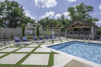 A swimming pool in front of a house with lounge chairs