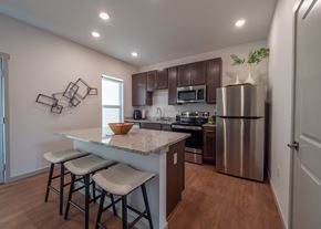 Springdale townhouse for rent - a kitchen with stainless steel appliances and a counter with three stools at The Row on Merchant Apartments, Springdale, Ohio